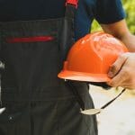 Man in overalls holds safety helmet outdoor